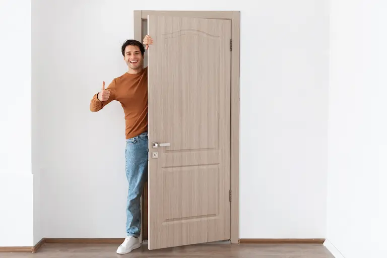 installation de portes alu bois ppvc asap fermetures (8) Homme souriant avec pouce levé derrière porte ouverte.