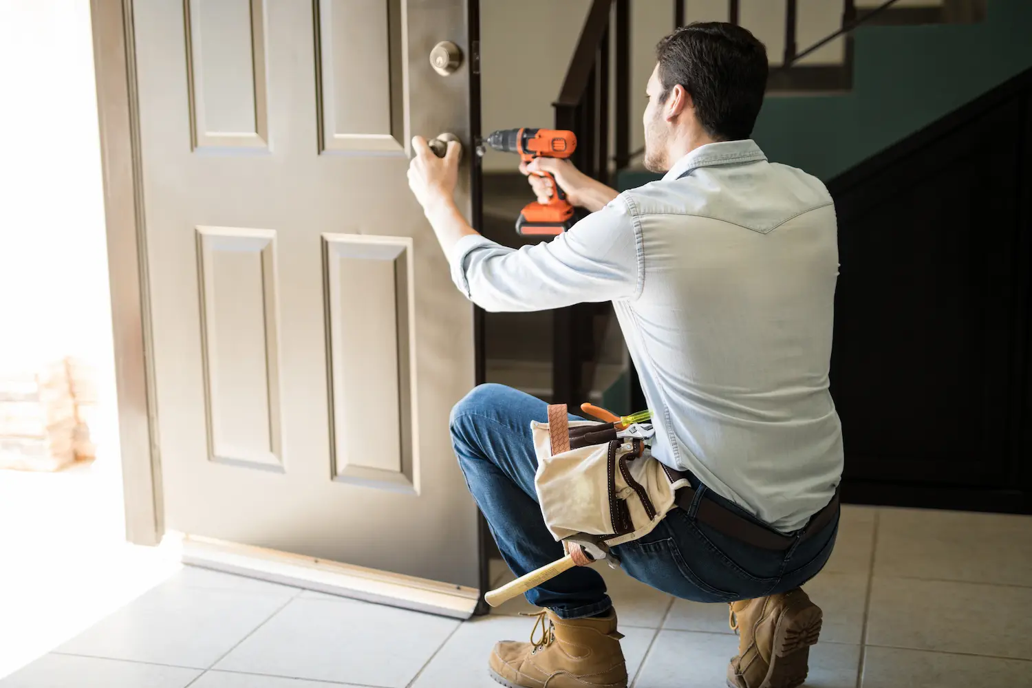 Homme réparant serrure de porte avec perceuse.