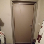Porte d'entrée beige dans un couloir sombre.