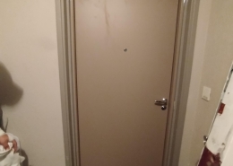 Porte d'entrée beige dans un couloir sombre.