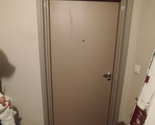Porte d'entrée beige dans un couloir sombre.