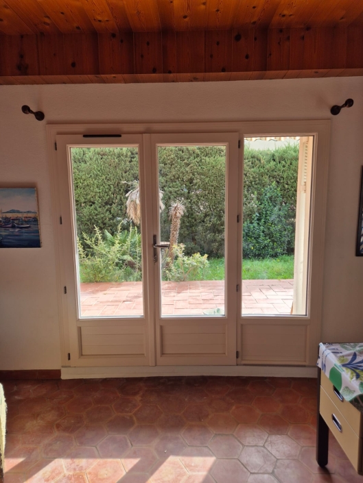 Porte-fenêtre ouvrant sur un jardin verdoyant.